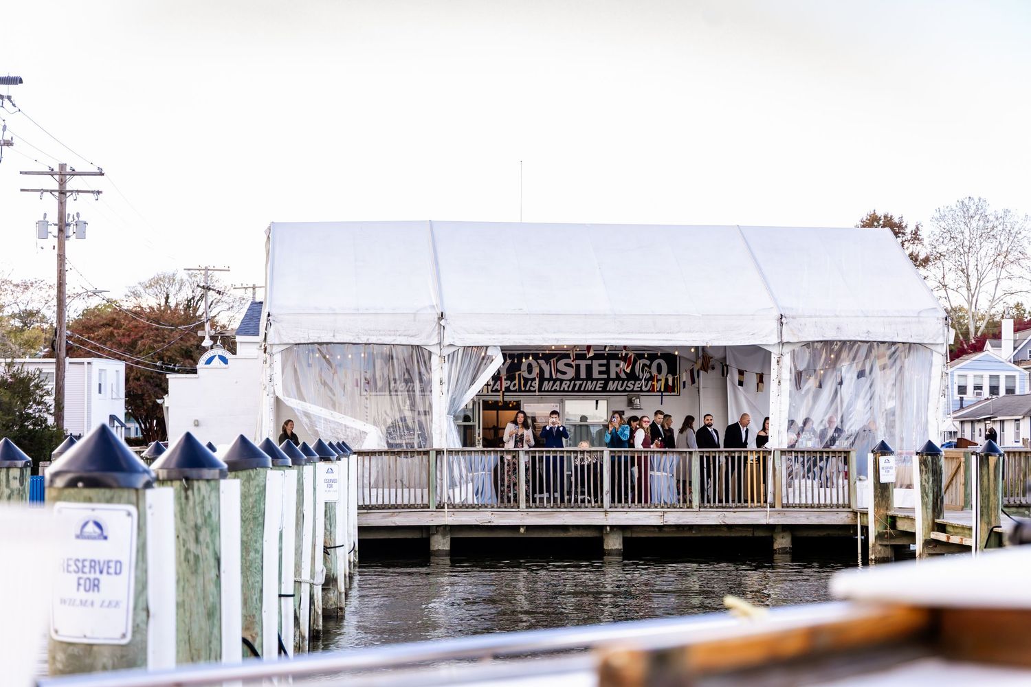 Waterfront Oyster Co. tent venue on a dock with guests dining, surrounded by calm harbor waters.