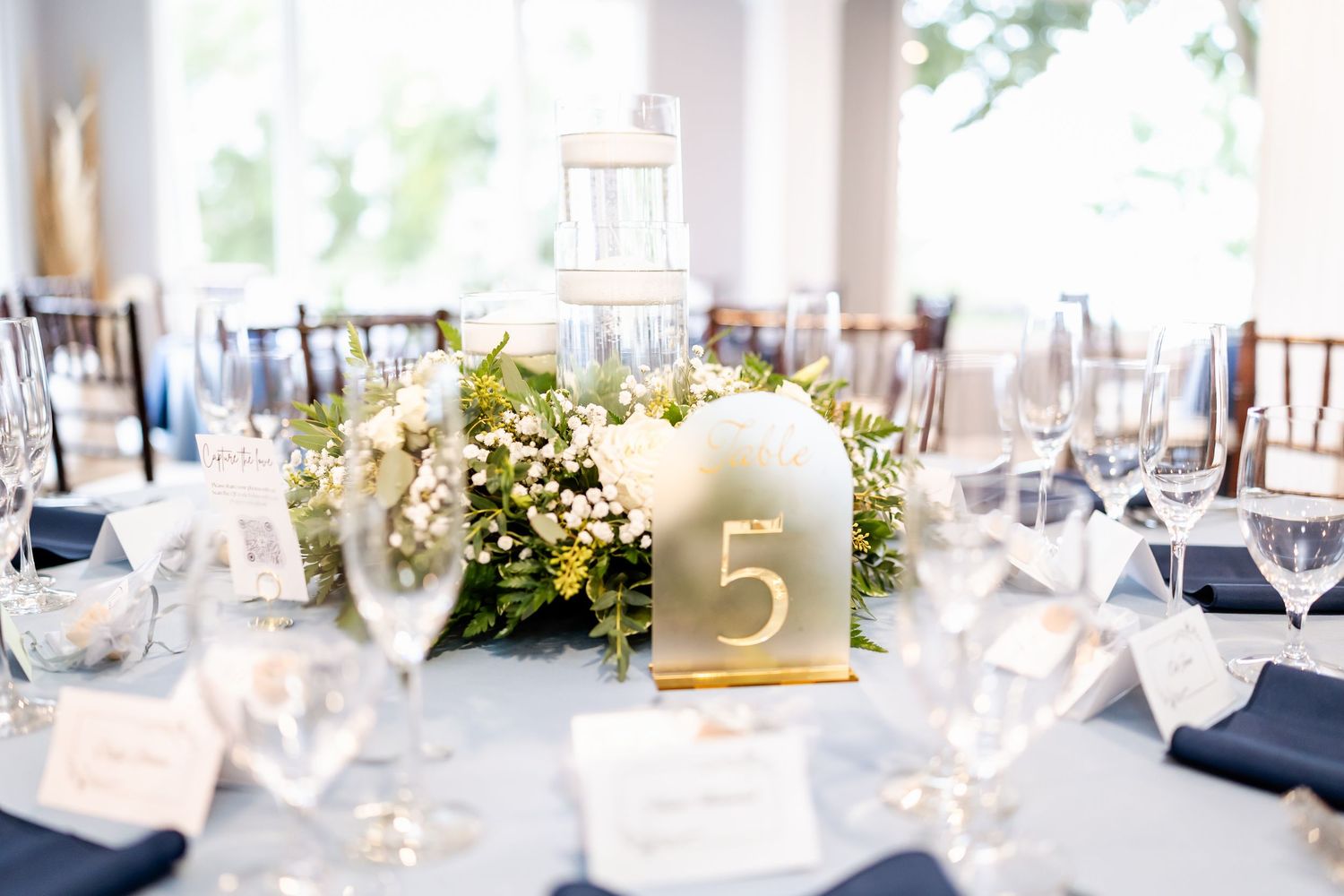 Elegant wedding reception tables set with navy and white decor, glassware and floral centerpieces.