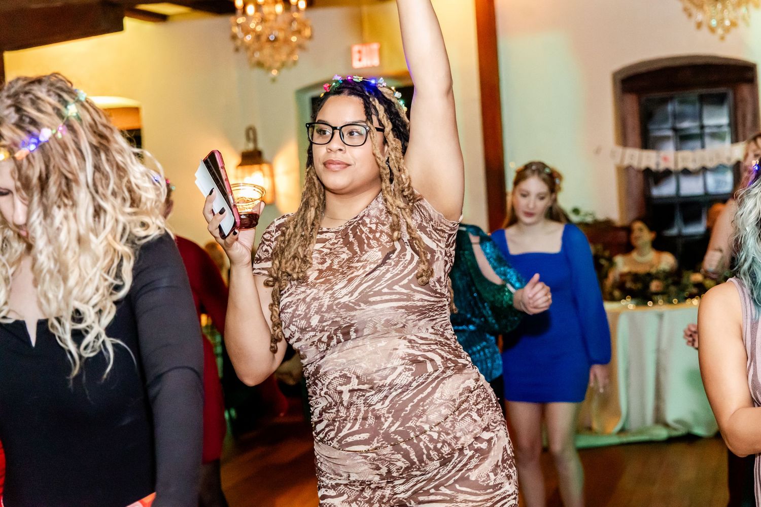 Wedding guests dancing and celebrating in a beautifully lit reception venue with chandeliers.