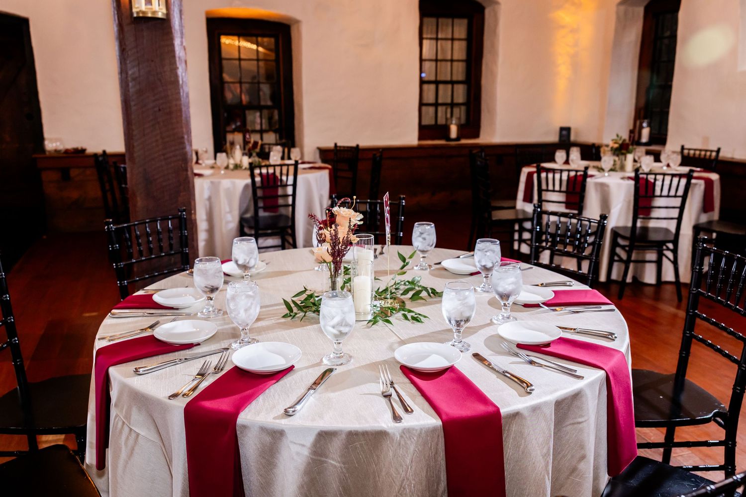 A formal wedding reception table set with white linens, burgundy accents, and classic place settings.