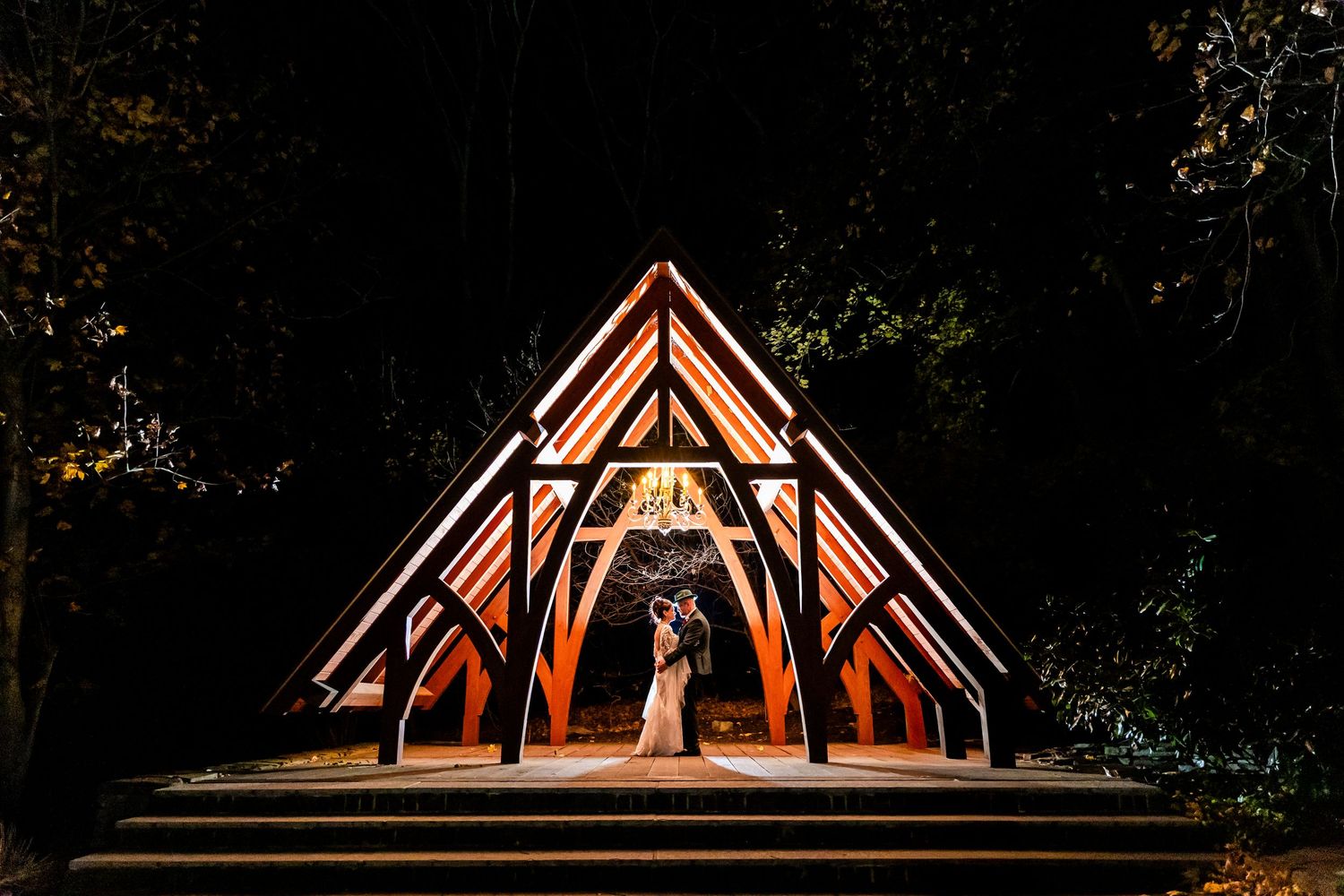 Illuminated wooden wedding arch glowing warmly against a dark night sky.