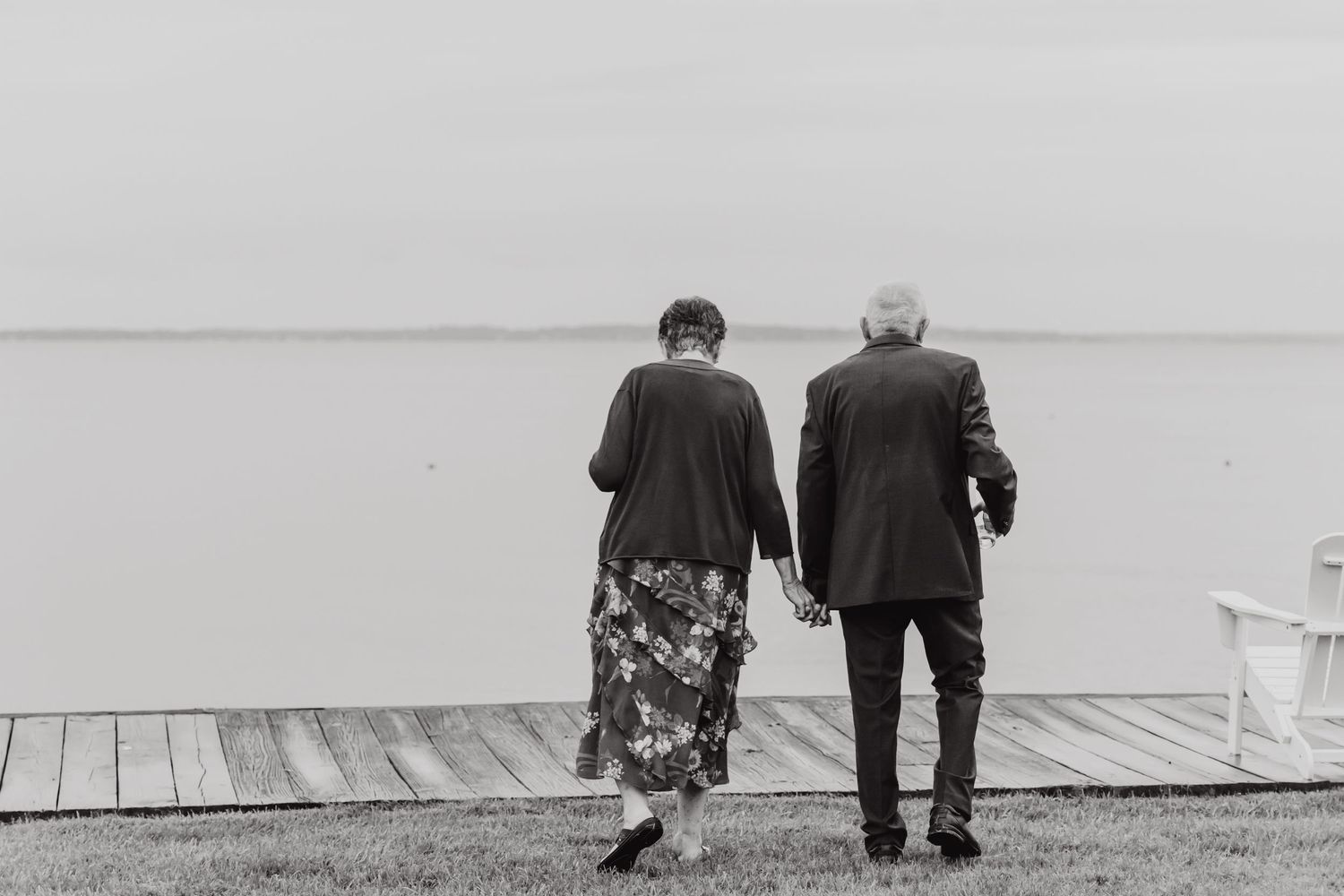 A black and white photo of two people sitting together on a dock overlooking water.