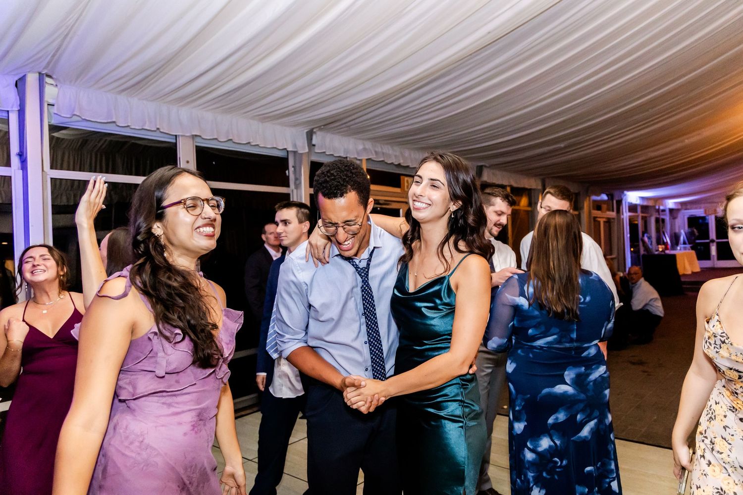 Wedding reception dance party with guests celebrating under draped ceiling and purple lighting.