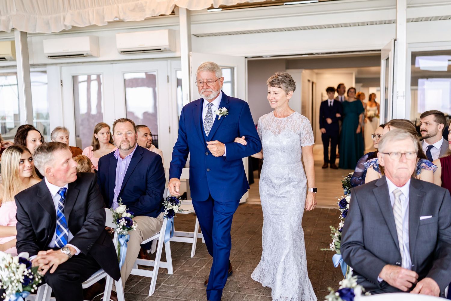 Wedding guests celebrate during an indoor reception with white decor and elegant table settings.