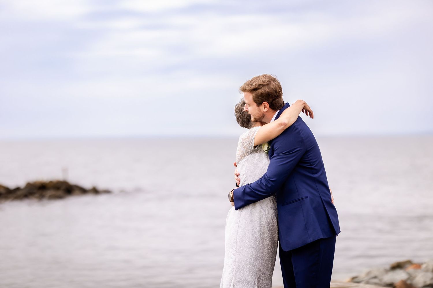 Romantic wedding couple embraces on a cloudy beach boardwalk in matching navy and white attire.