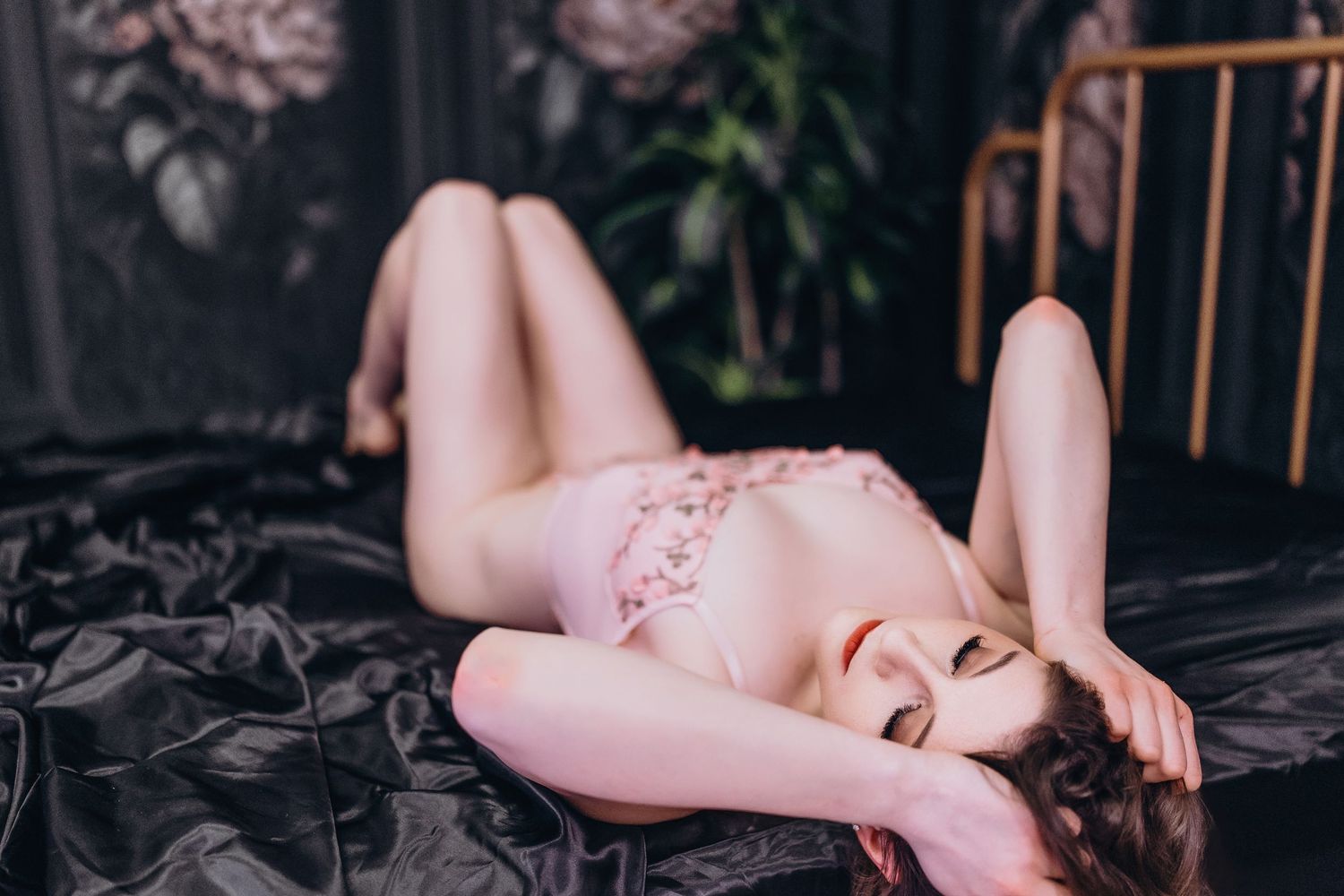 Person reclining on dark bedding with copper or rose gold colored bed frame visible in background.