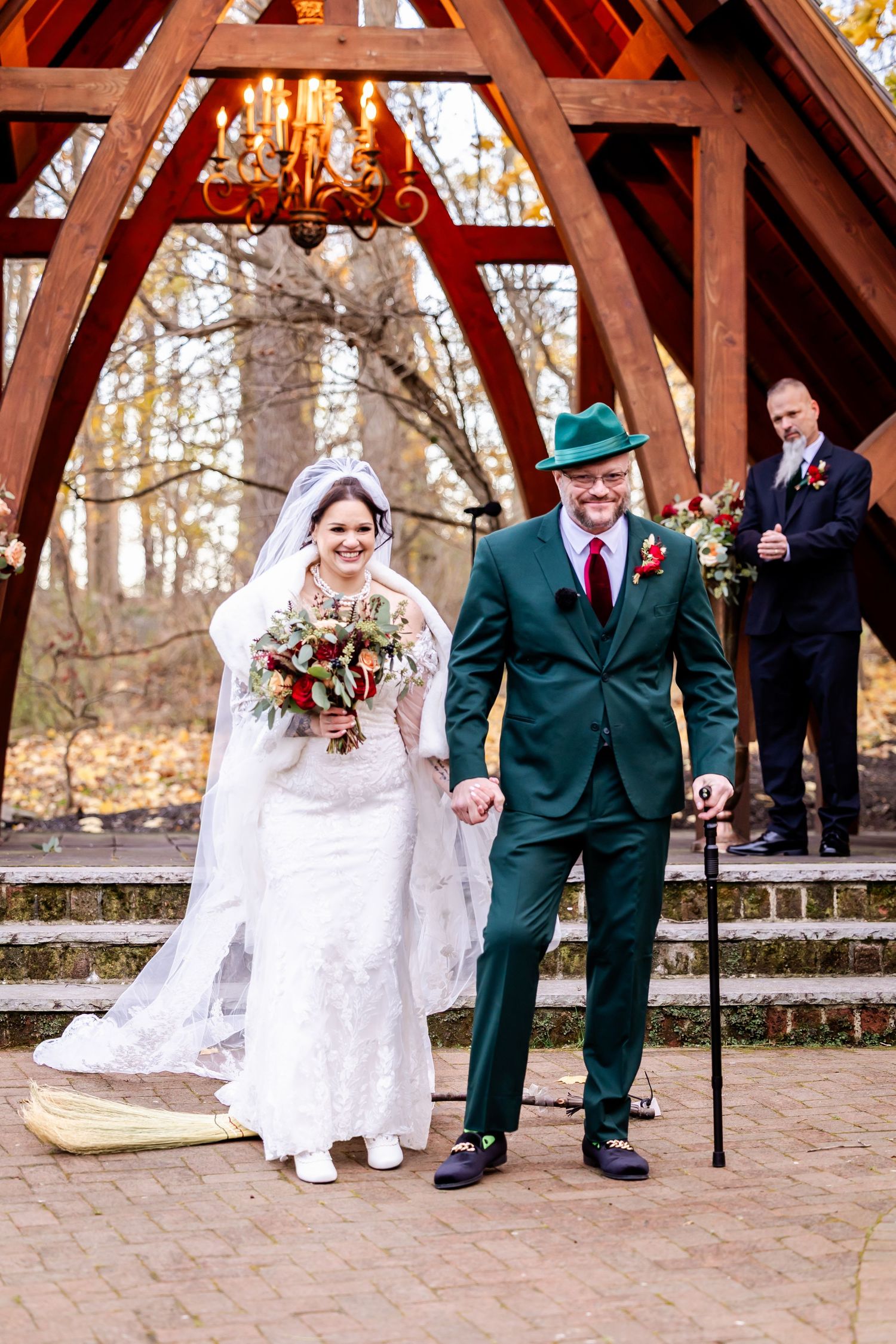 A wedding ceremony under a rustic wooden pavilion with autumn trees in the background.