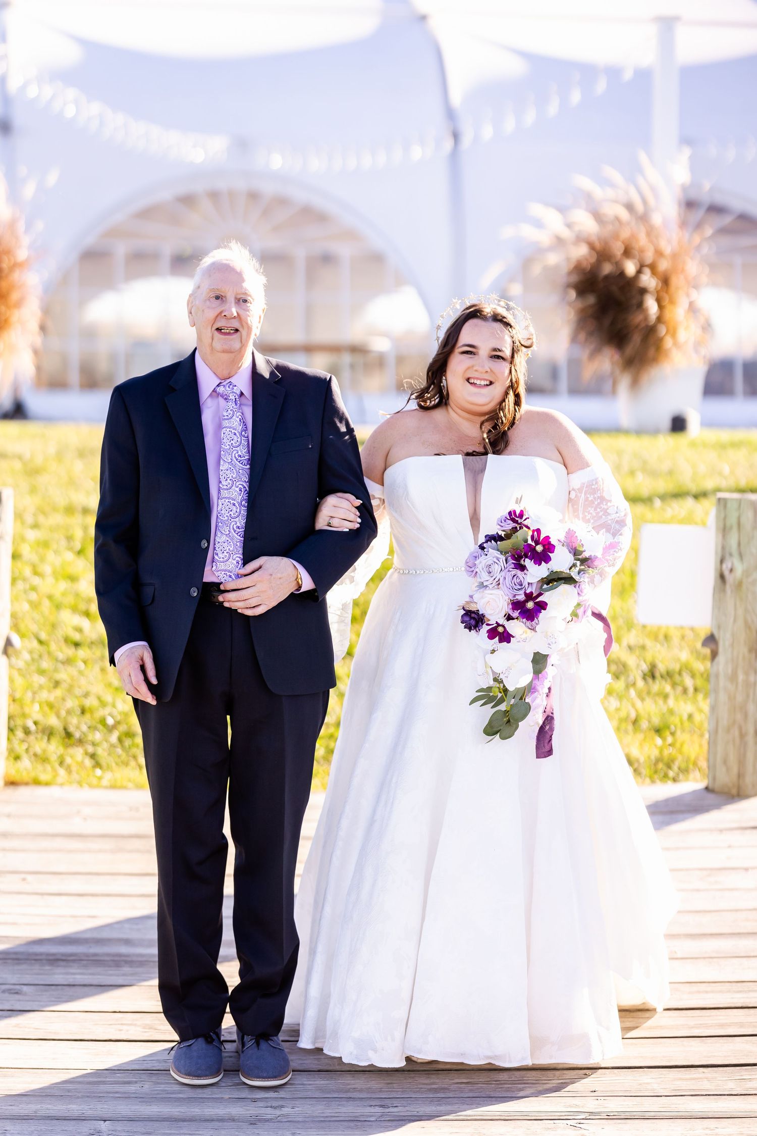 Wedding pair standing on wooden boardwalk under white tent canopy with bright autumn decor.