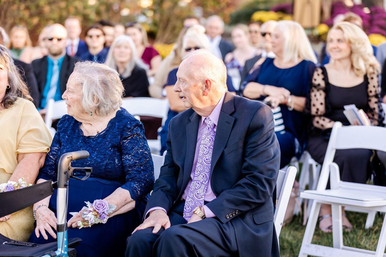 Wedding guests seated in white chairs during an outdoor ceremony with natural landscaping.