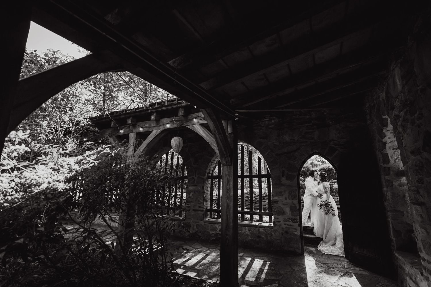A wedding photoshoot under an arched stone structure creating dramatic shadows and lighting.