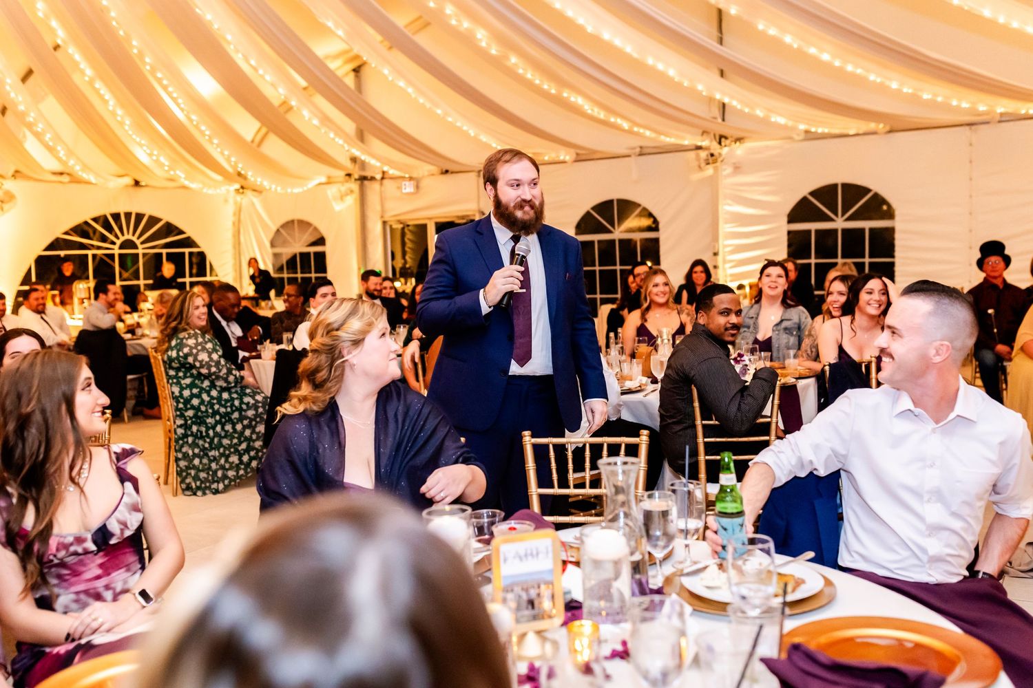 Wedding speech being delivered in tent venue with guests seated at round tables.