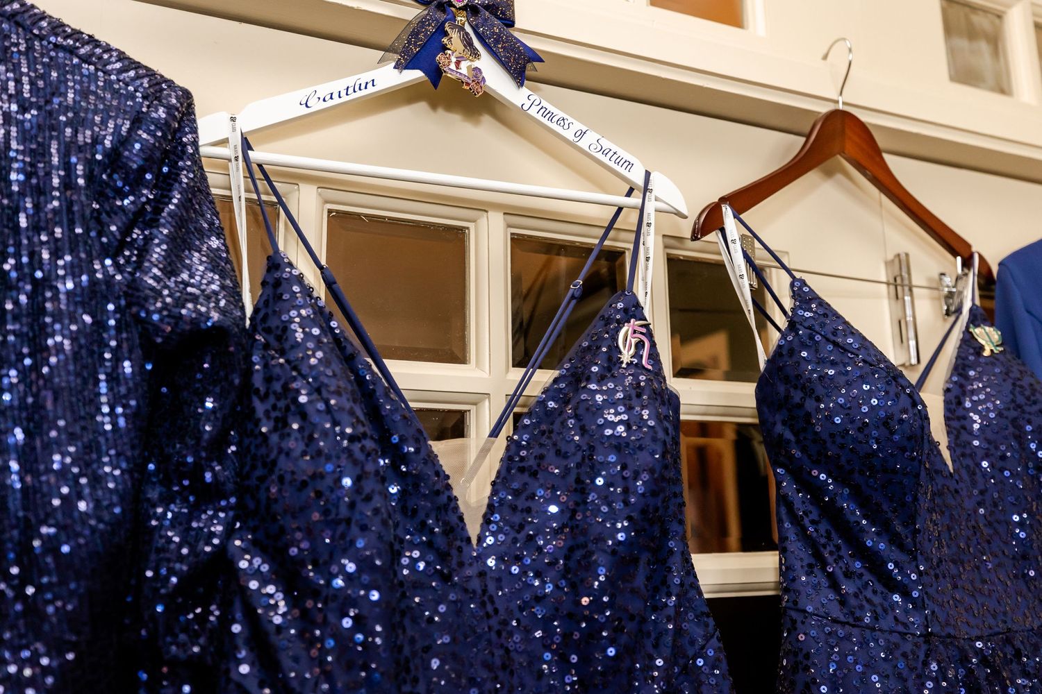 Close up of navy sequined formal dresses hanging on wooden hangers.