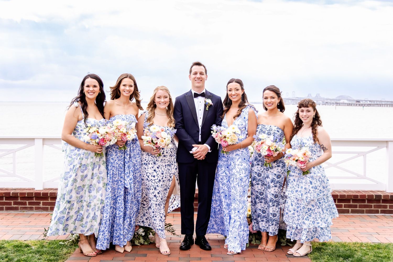 Wedding party in coordinated blue floral dresses posed on brick terrace.