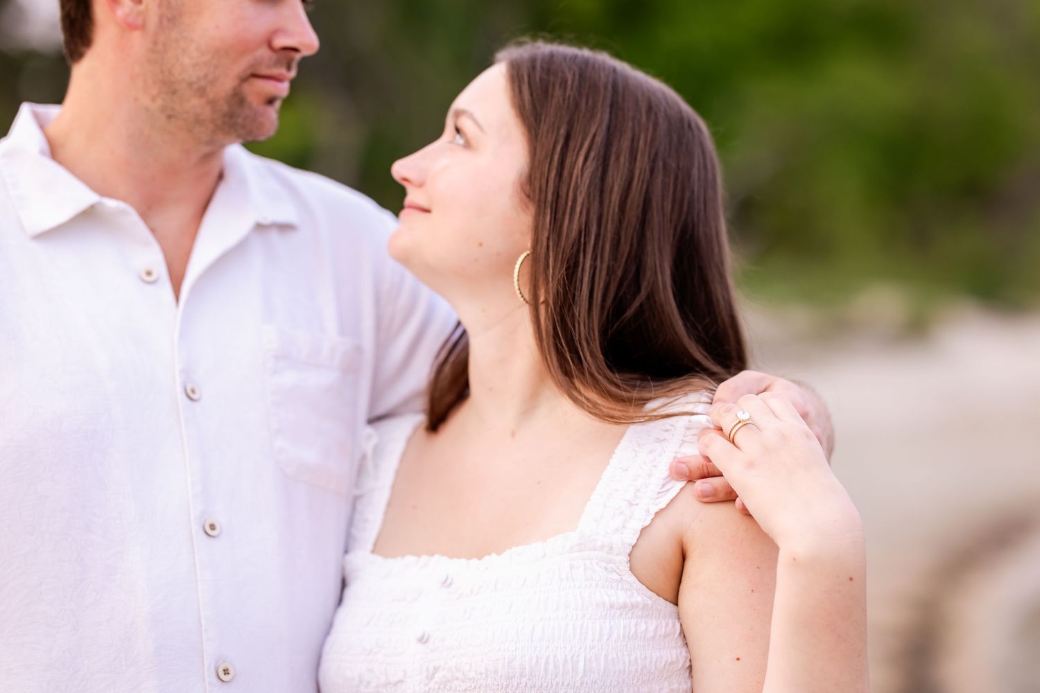 A couple in white attire sharing intimate romantic moments during an outdoor engagement photo session.