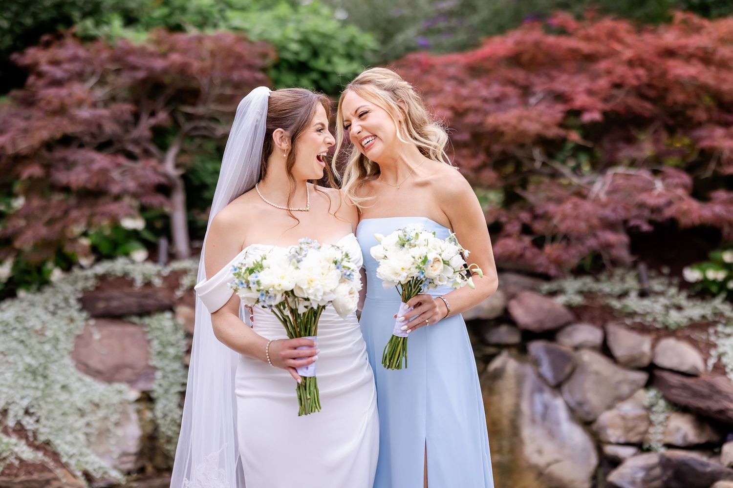 Bridesmaids in light blue dresses hold white bouquets while standing together outdoors.