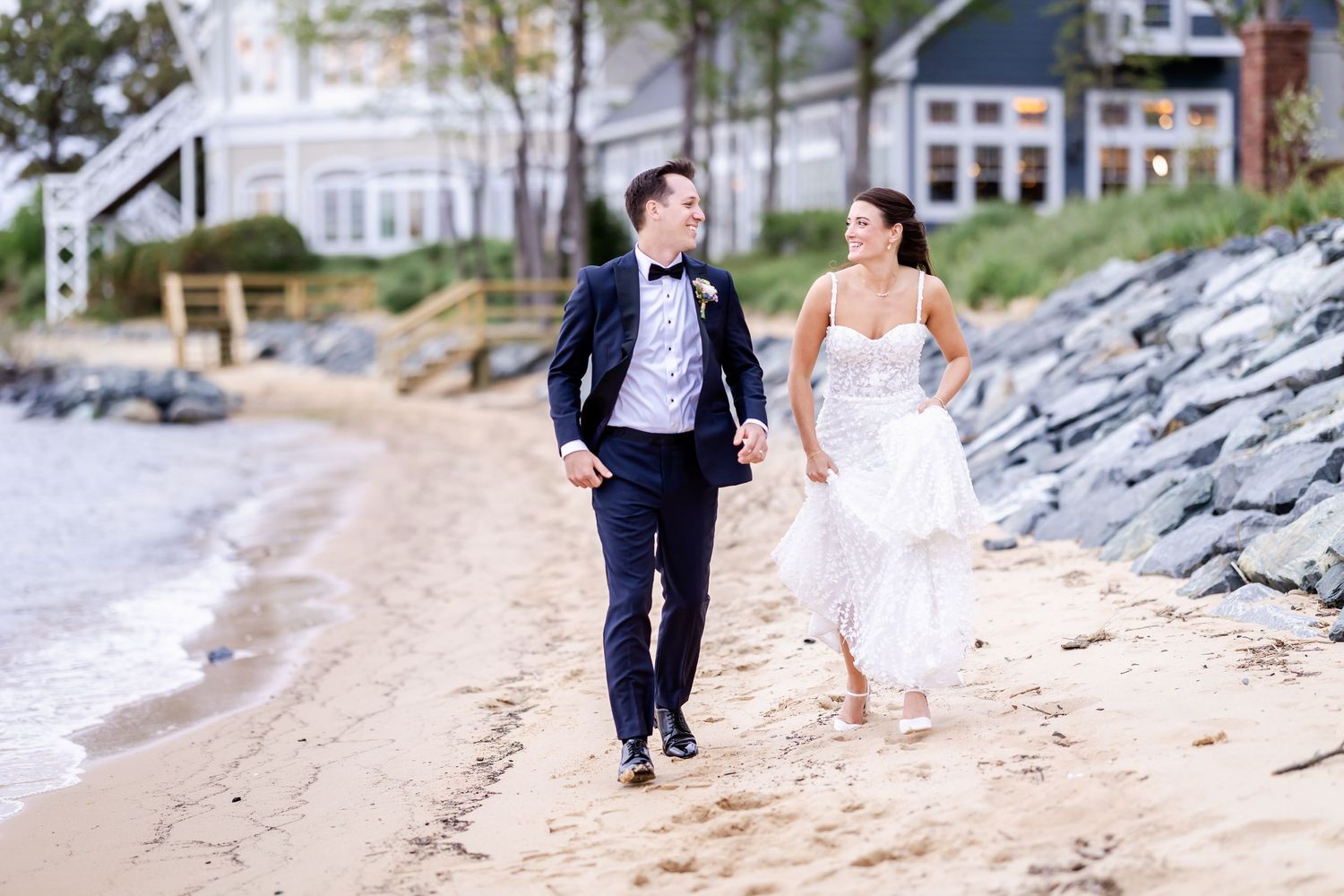 A couple runs joyfully along the shoreline during their wedding photoshoot.