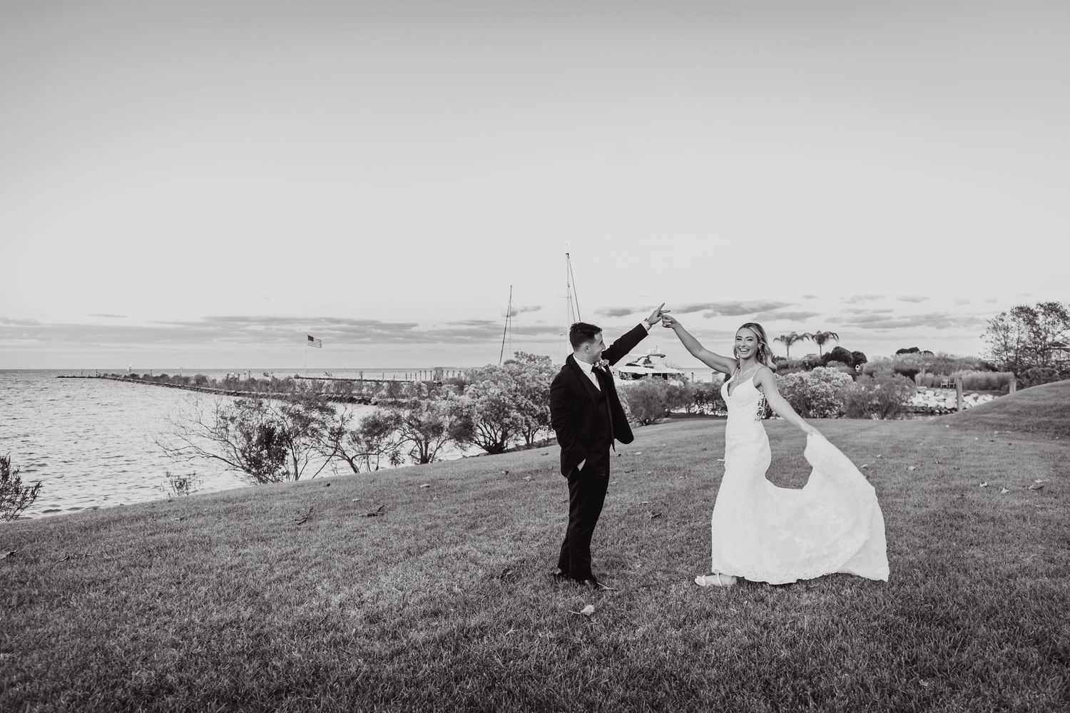 Black and white photo of bride and groom posing playfully on hilltop overlooking landscape.