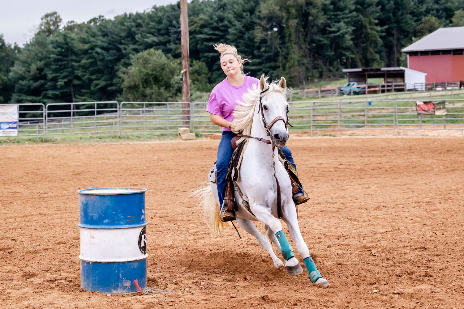 Equestrian rider practicing barrel racing patterns around blue drums in a dirt arena.
