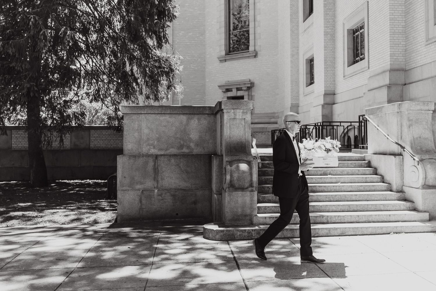 A black and white photograph of someone ascending stone steps beside a white building on a sunny day.