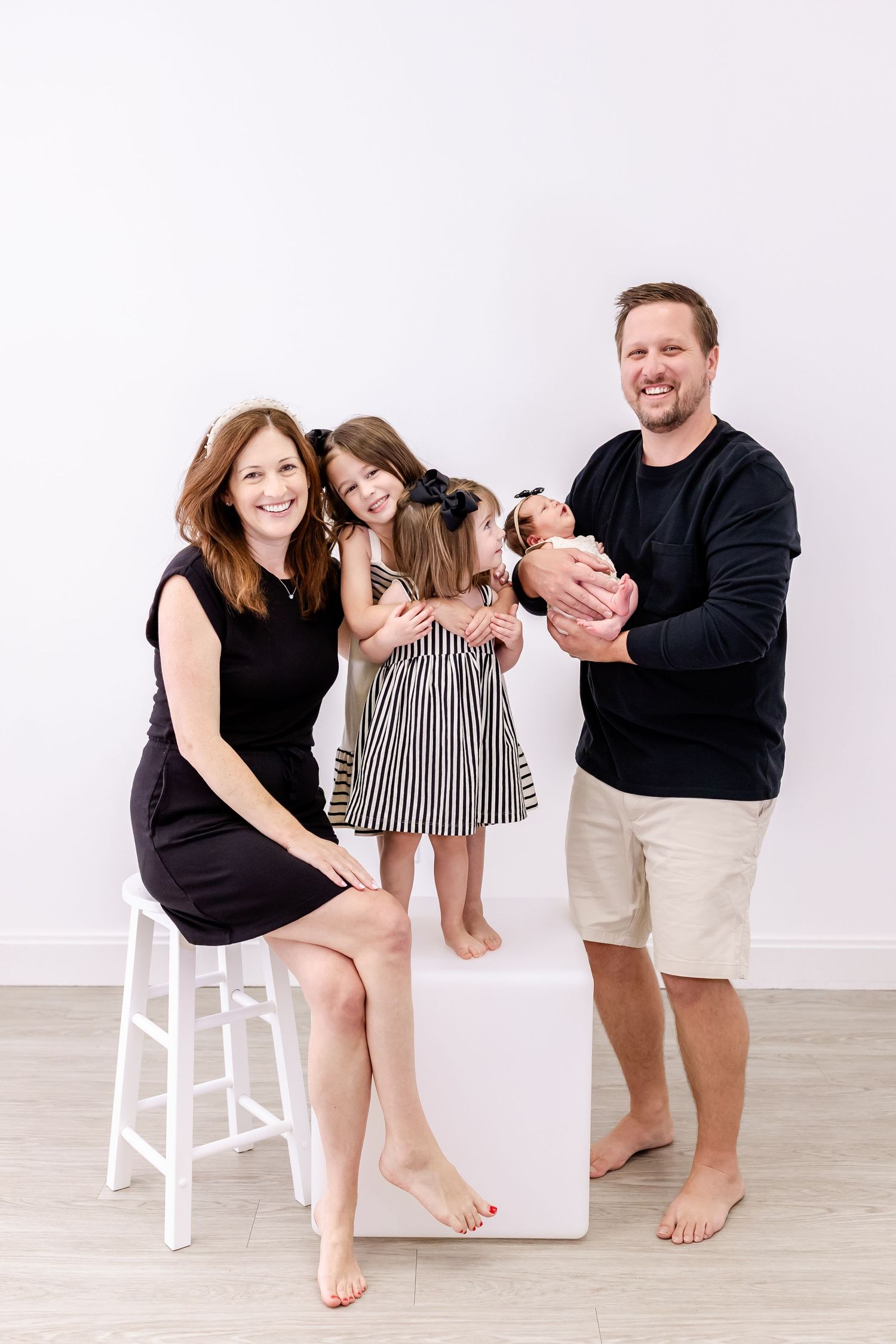 A playful family photo sequence showing barefoot poses in black and white outfits on a white wood floor.