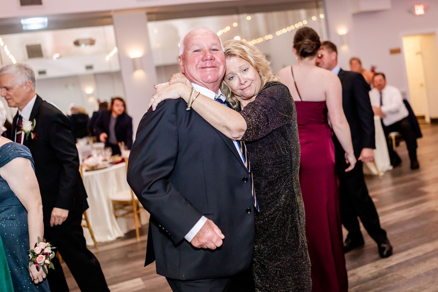 Wedding guests dance and celebrate together in a bright modern reception hall with string lights.