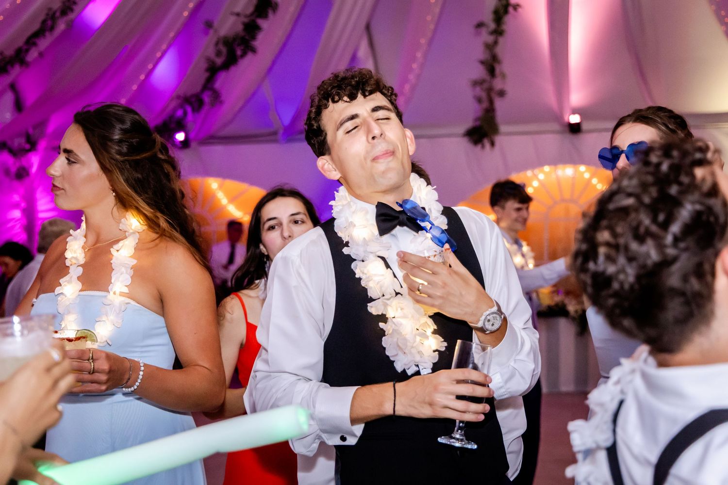 Wedding reception guests dancing and celebrating on a dance floor illuminated with purple lighting.
