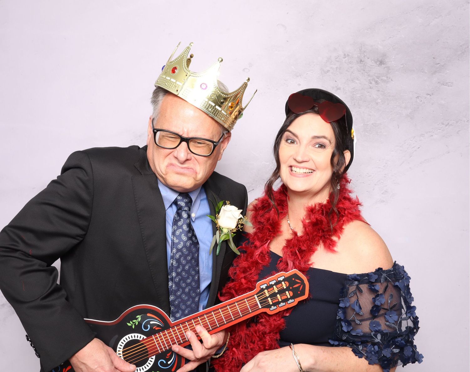 Couple poses playfully with a red guitar during a wedding photo session against a white backdrop.