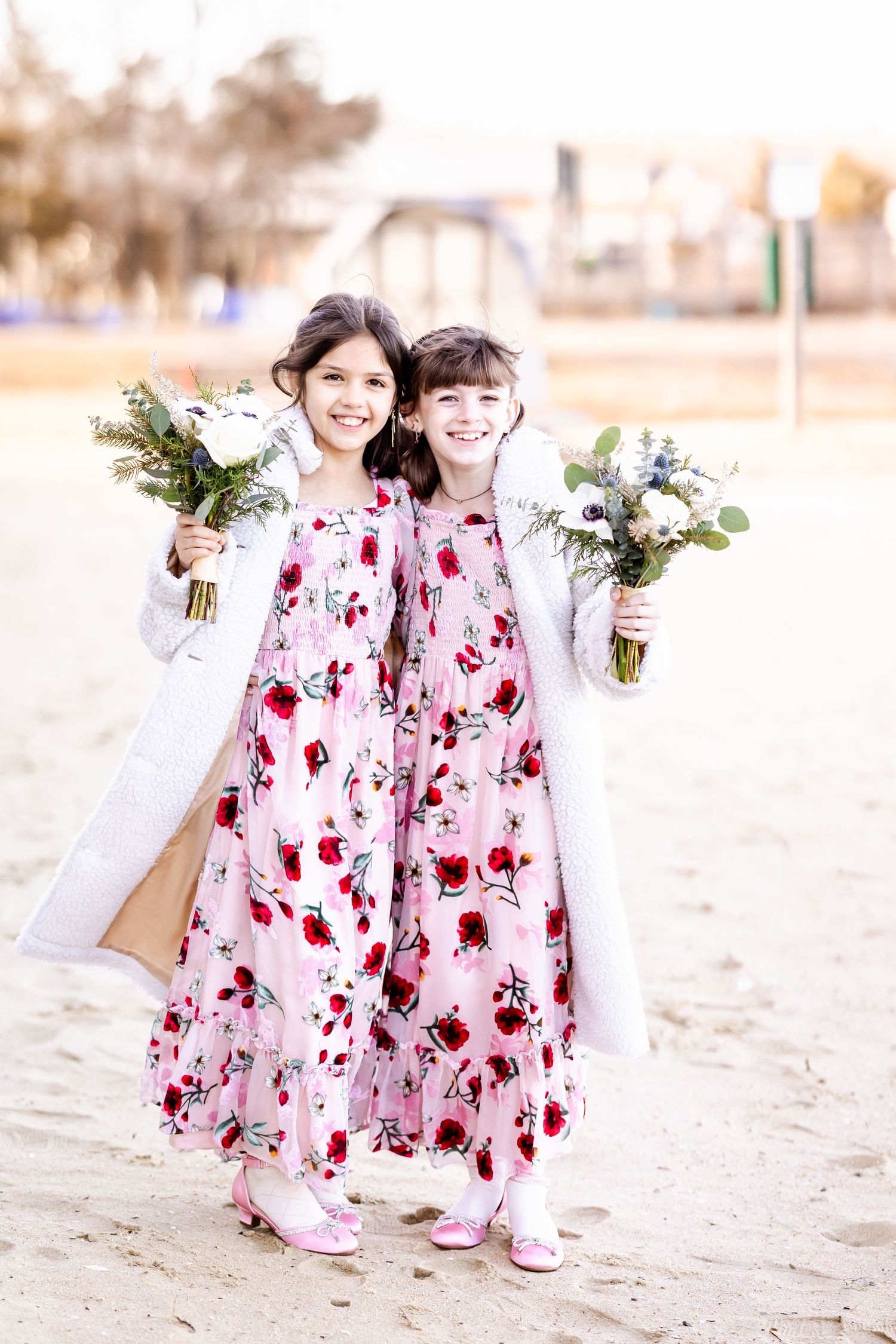 Two attendants in matching floral dresses hold bouquets while standing outdoors.