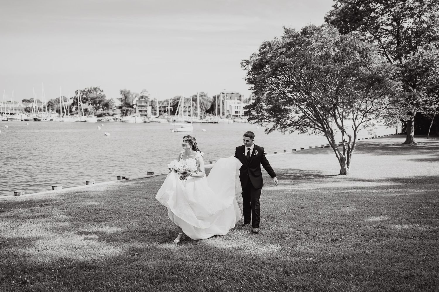 Black and white wedding photos captured along a scenic waterfront with dramatic sky.