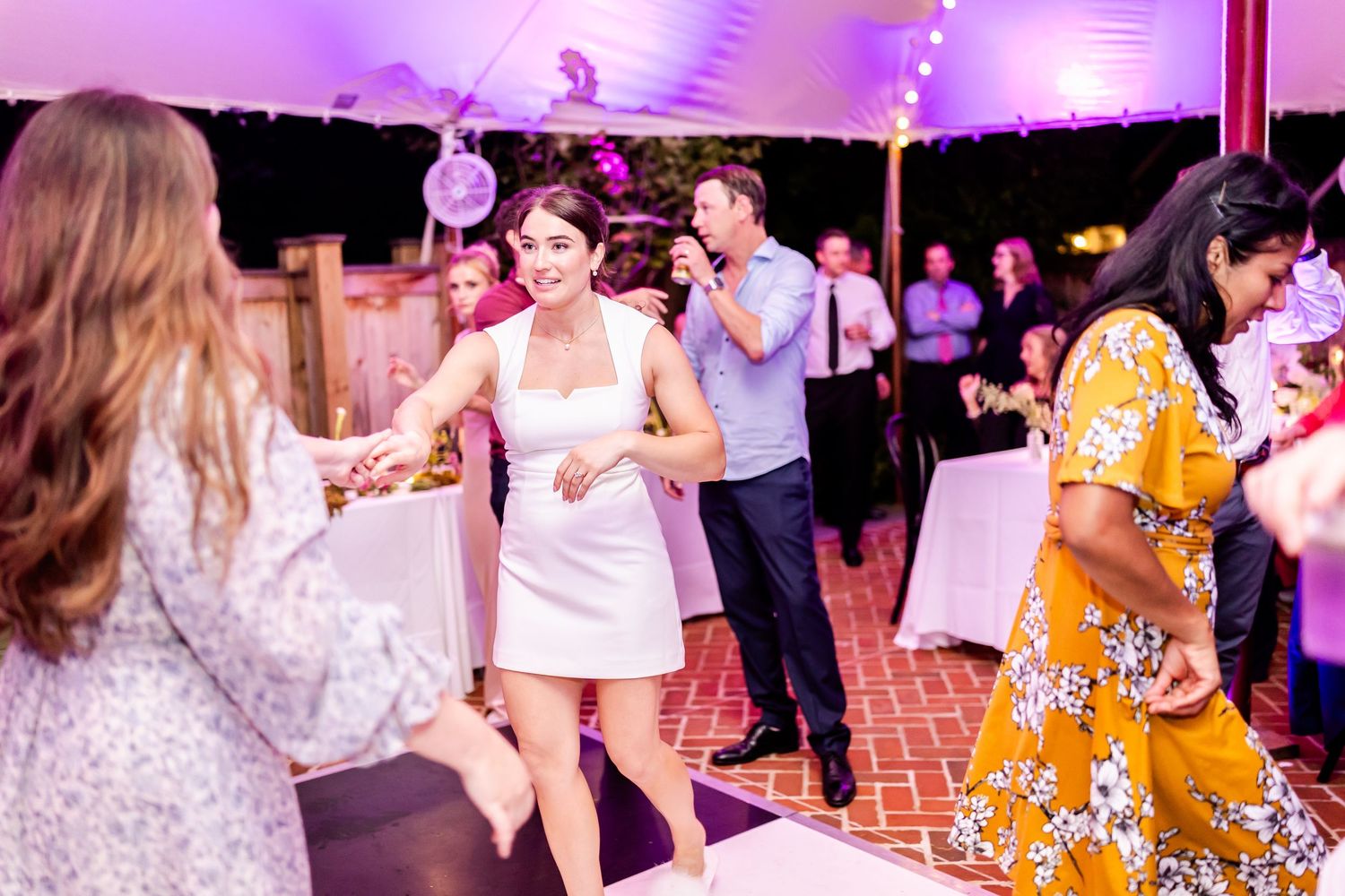 Wedding reception dance party with guests enjoying themselves under purple tent lighting.