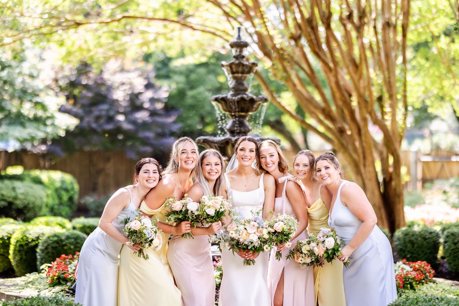 Wedding party gathers outdoors in a garden setting with decorative lanterns and floral arrangements.