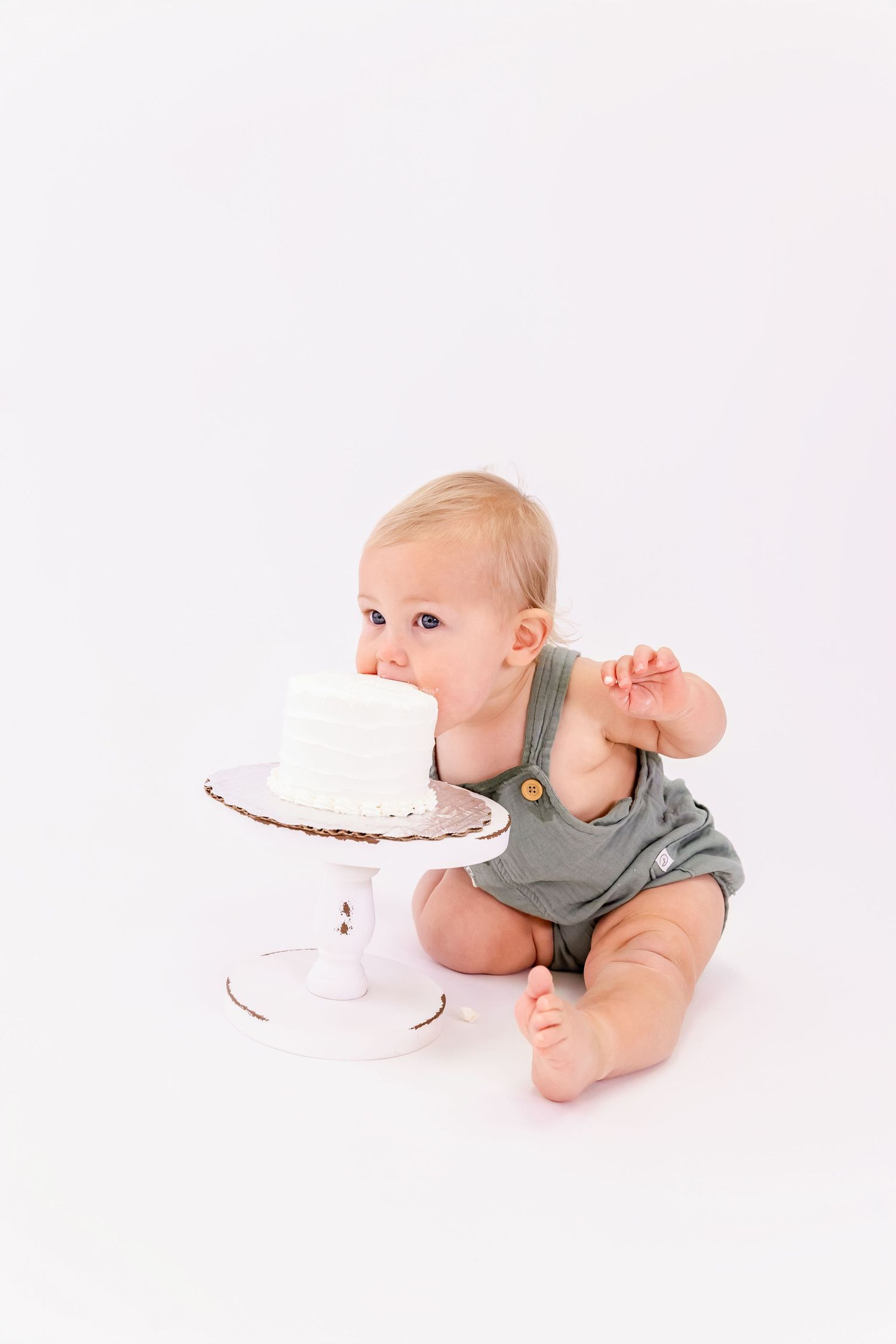 Baby in gray onesie crawling and reaching toward white cake on light background in sequential action shots.