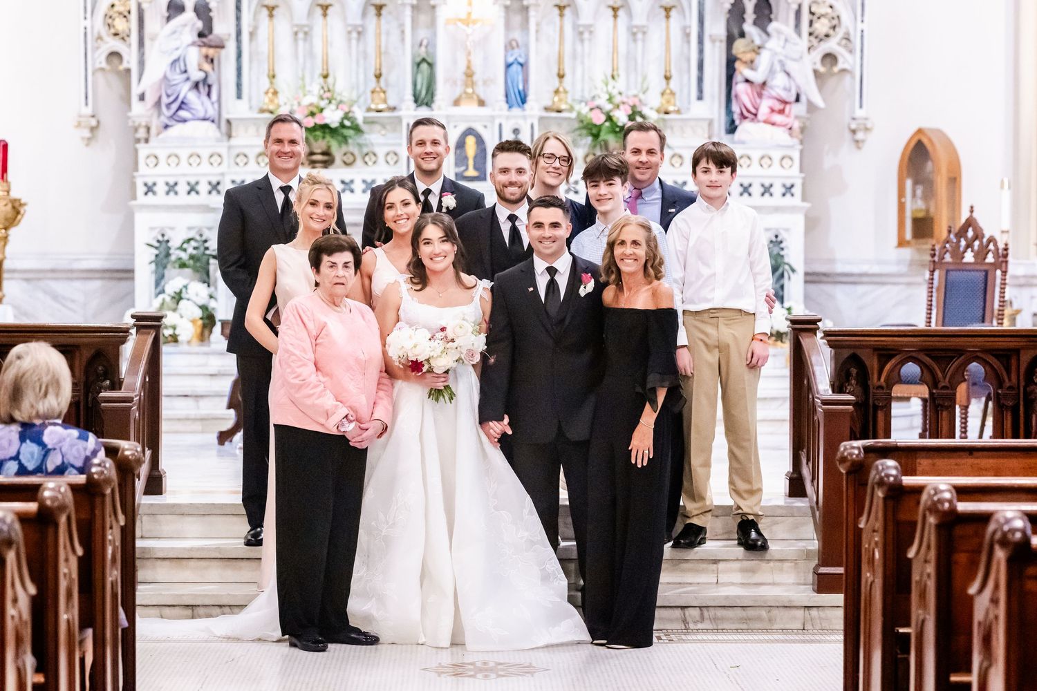 Wedding party poses together in front of ornate white church altar during formal ceremony.