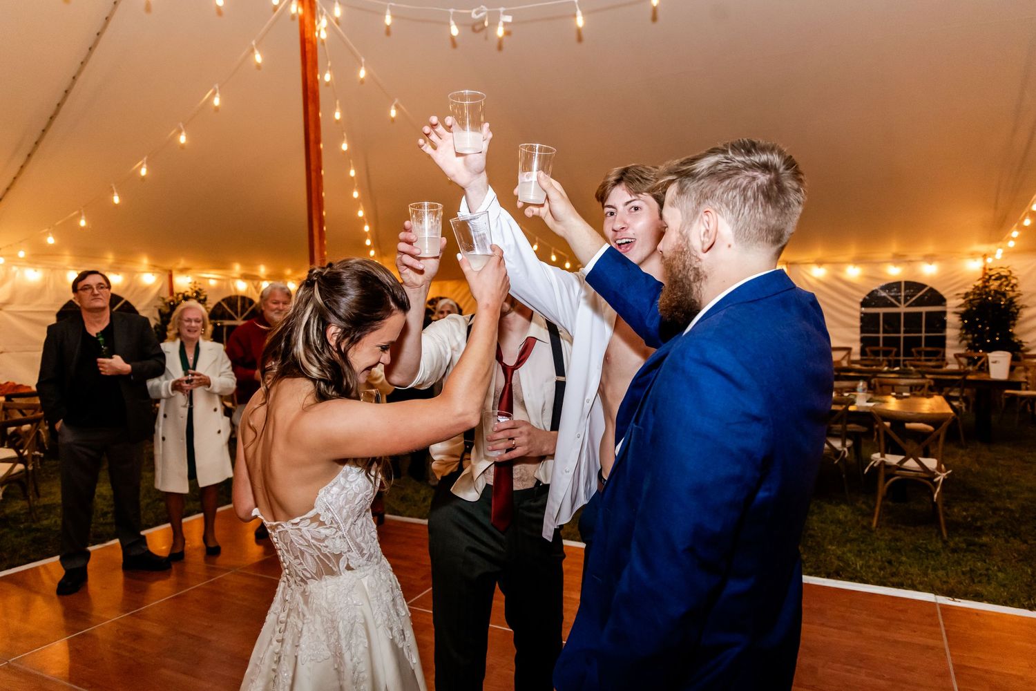 Wedding reception dance party under string lights in a tent venue.