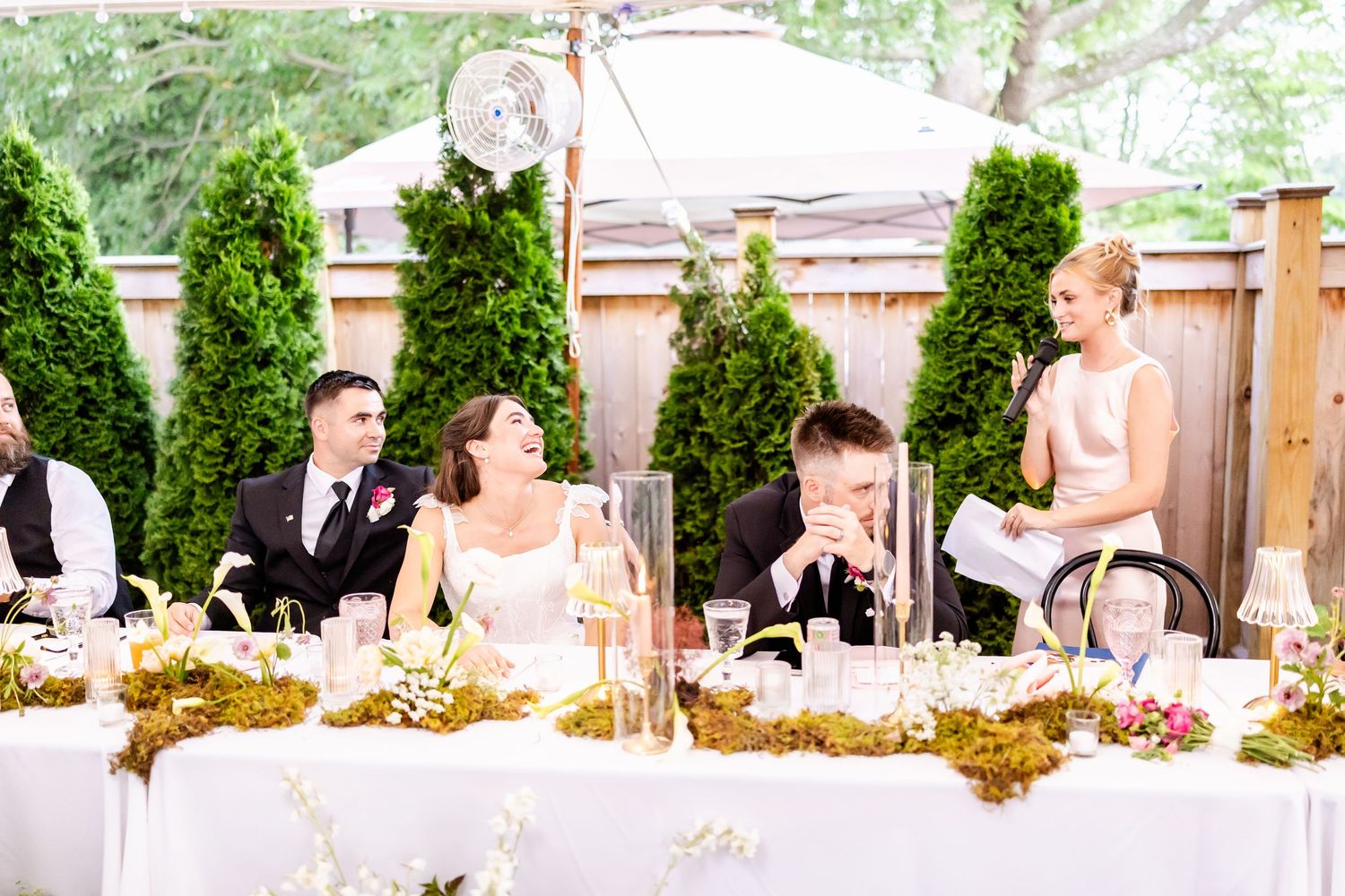 Wedding guests dance and celebrate on an outdoor dance floor under string lights and greenery.