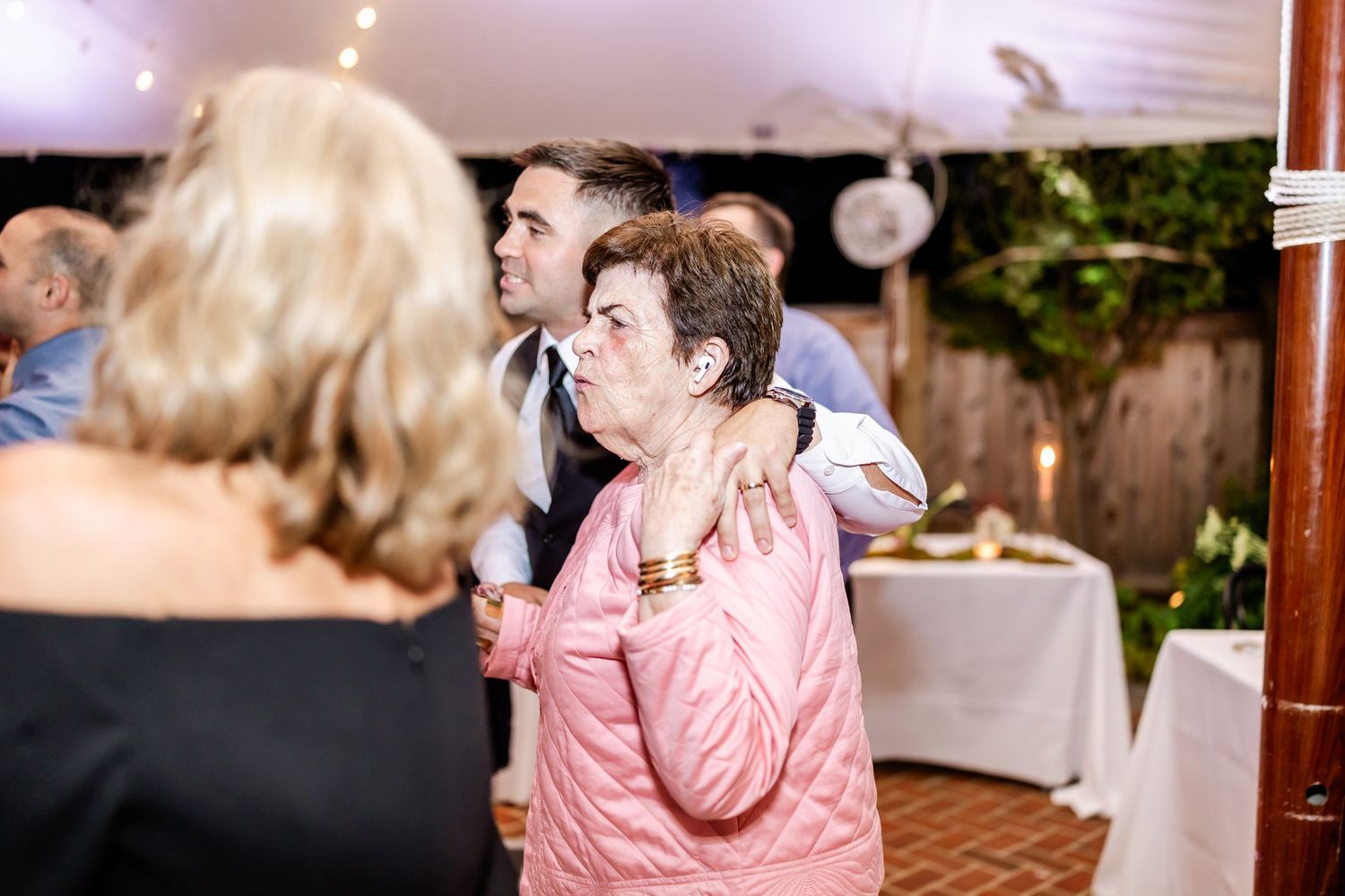 Wedding guests dancing and celebrating at reception under pink ambient lighting.