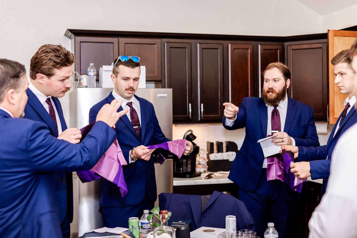 Group in navy blue suits gathered in a kitchen holding purple accessories.