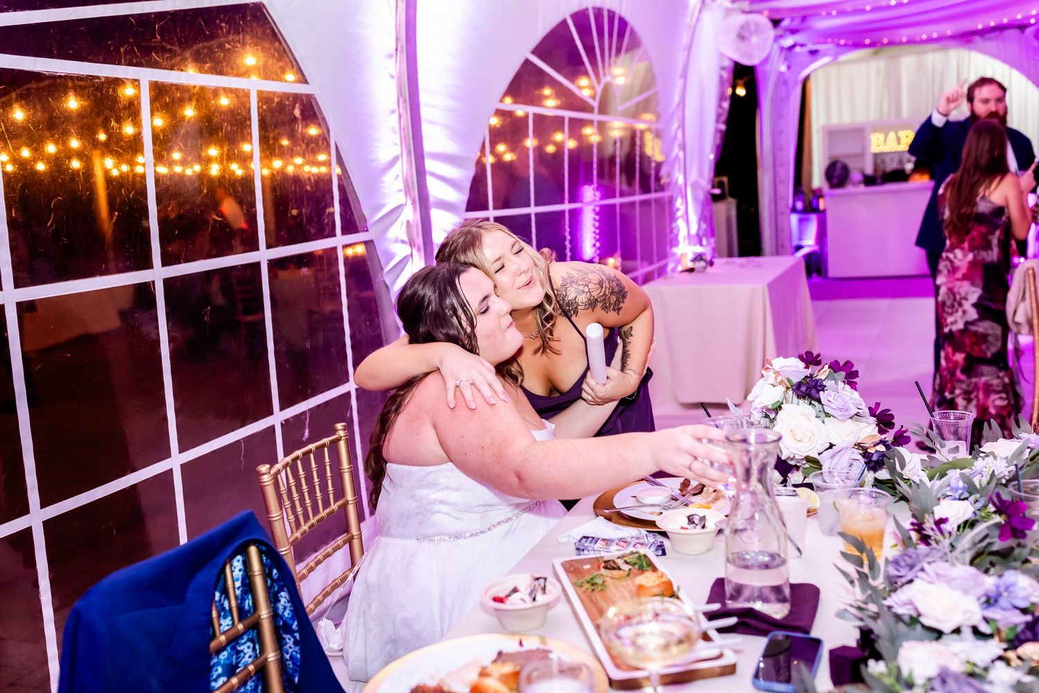 Wedding reception table setting with purple ambient lighting and decorative white fabric ceiling draping.