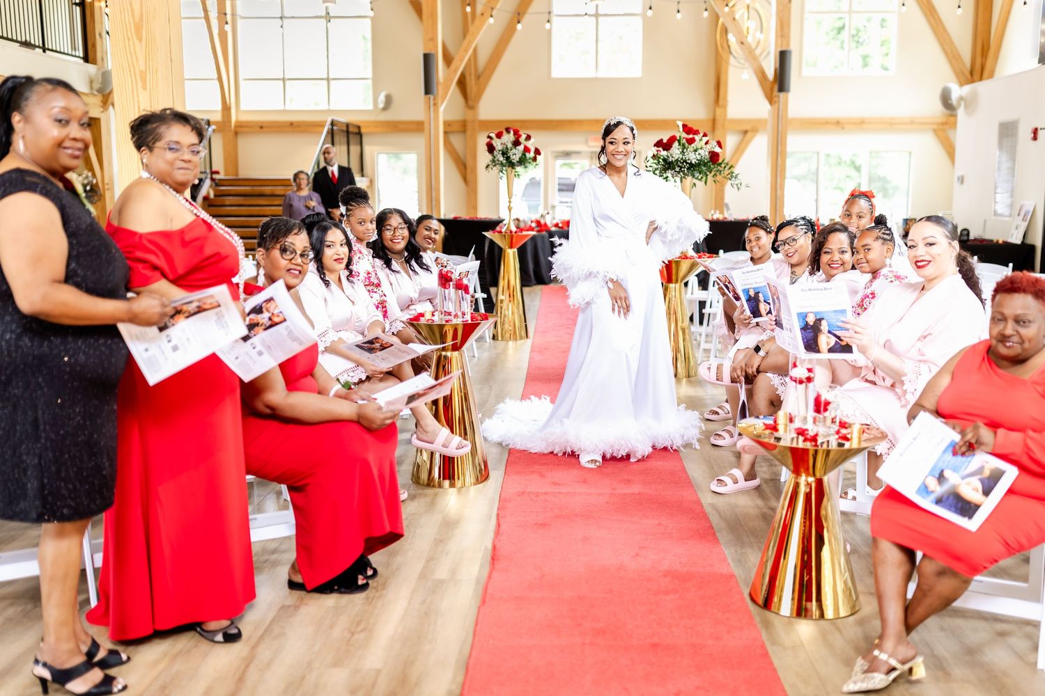 Wedding ceremony in a rustic venue with red dresses and white decor along a red carpet aisle.
