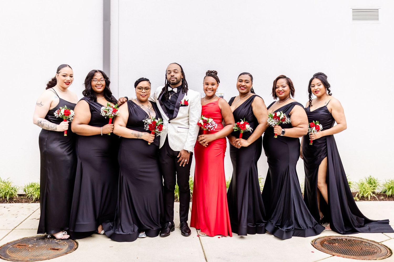 Wedding party in black dresses and one red gown pose together outdoors.
