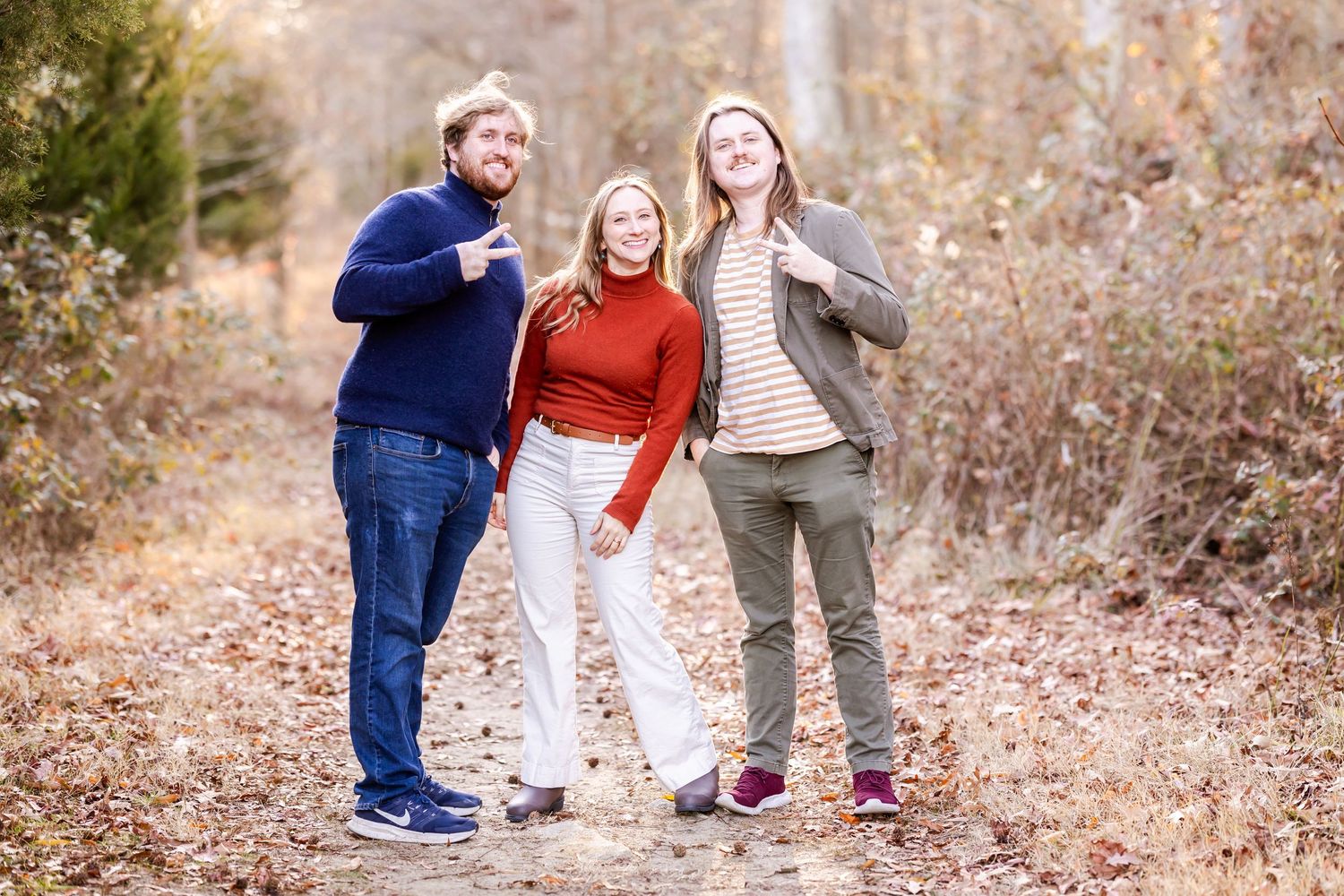 Three people laughing and having fun together while posing on an autumn nature trail.