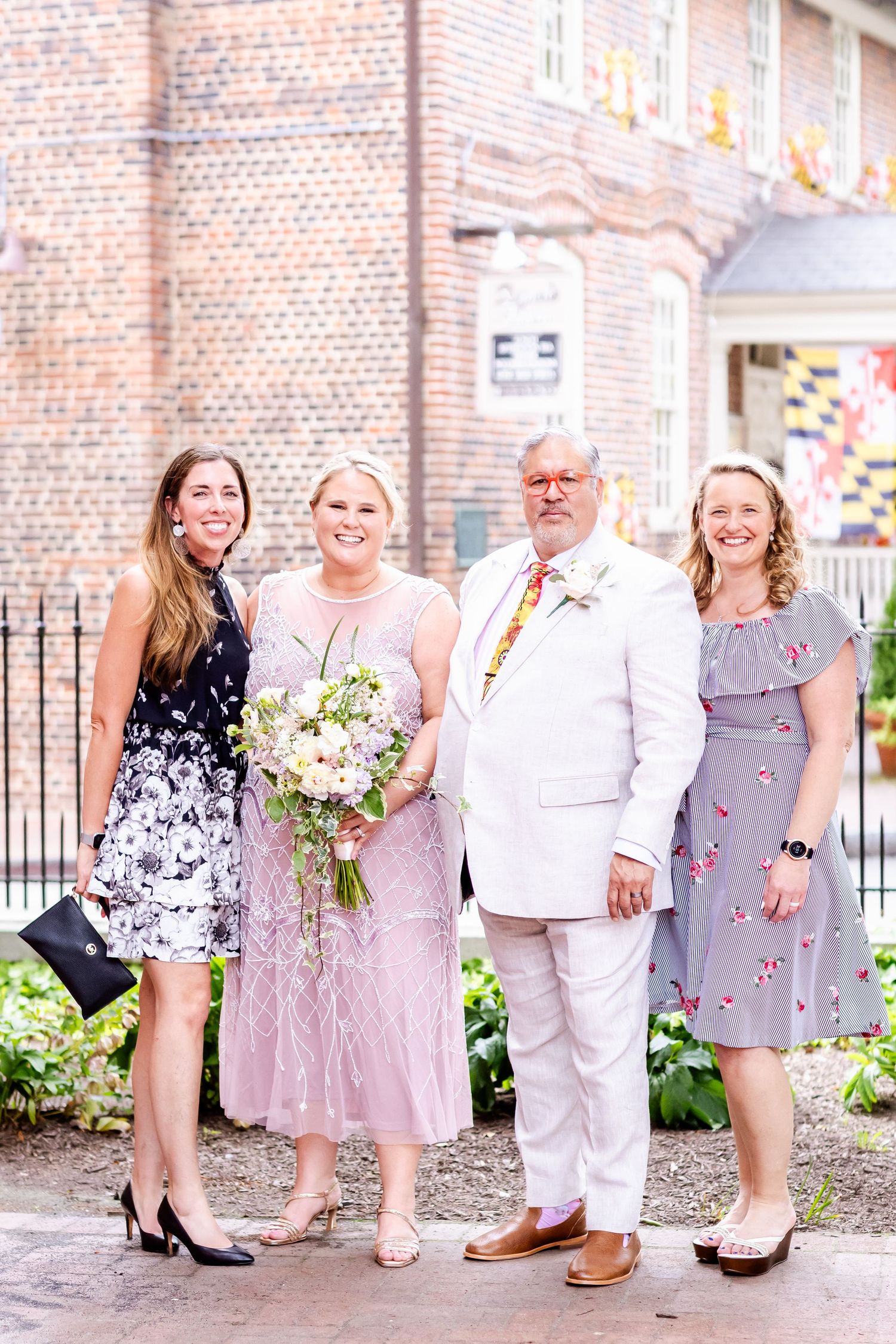 Small wedding group photo outdoors with brick building and Maryland flag decorations.