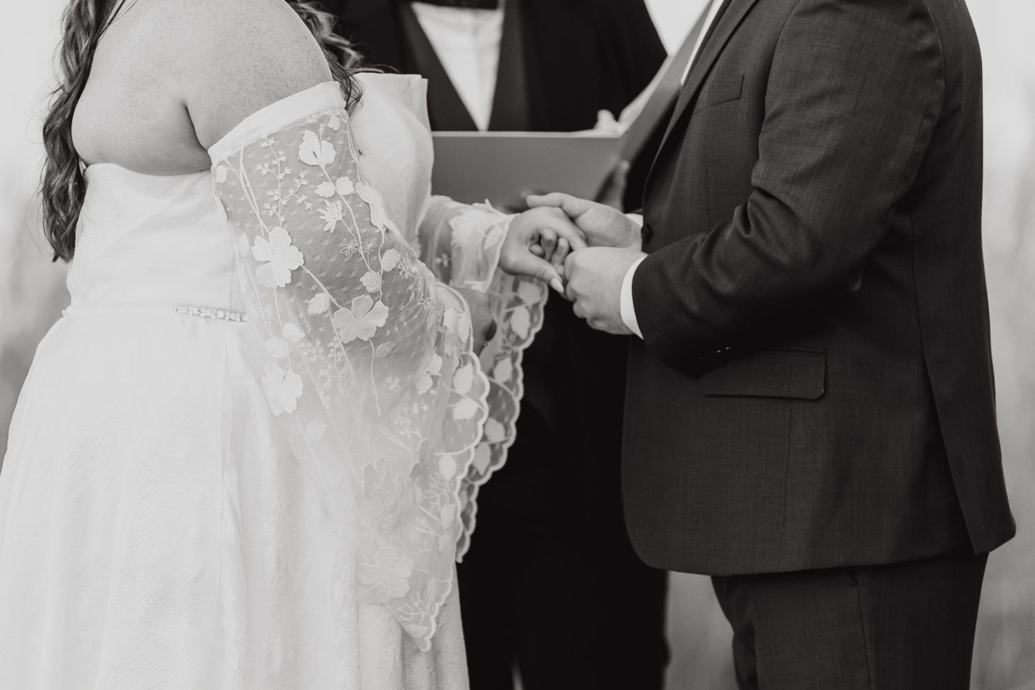 Close-up black and white shot of couple exchanging rings during wedding ceremony.