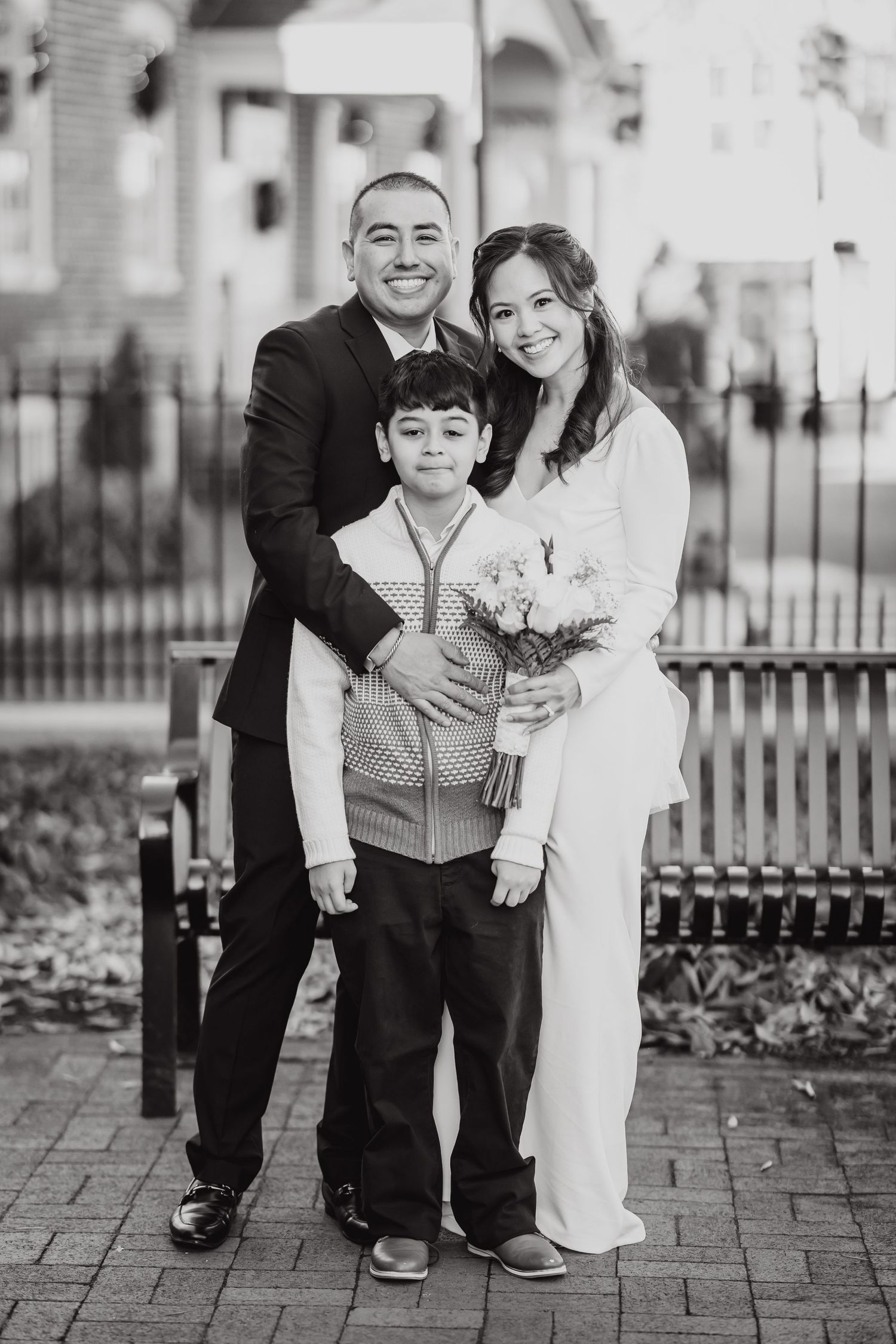 Black and white wedding portrait of three people standing on brick pavement.