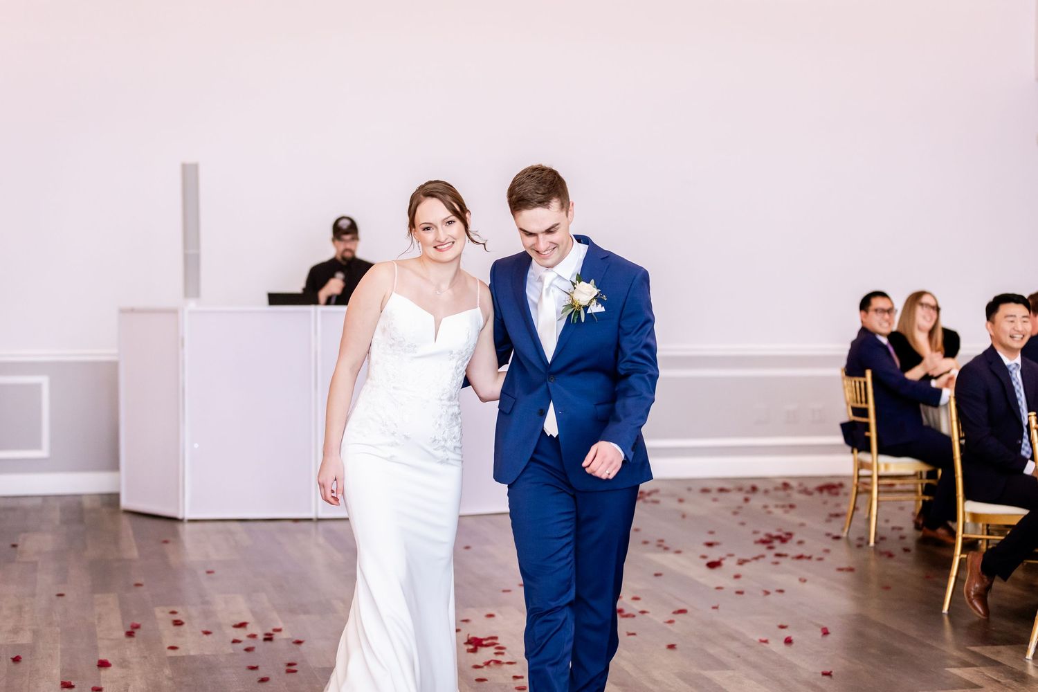 Wedding celebration scene with rose petals scattered on floor in bright indoor venue.
