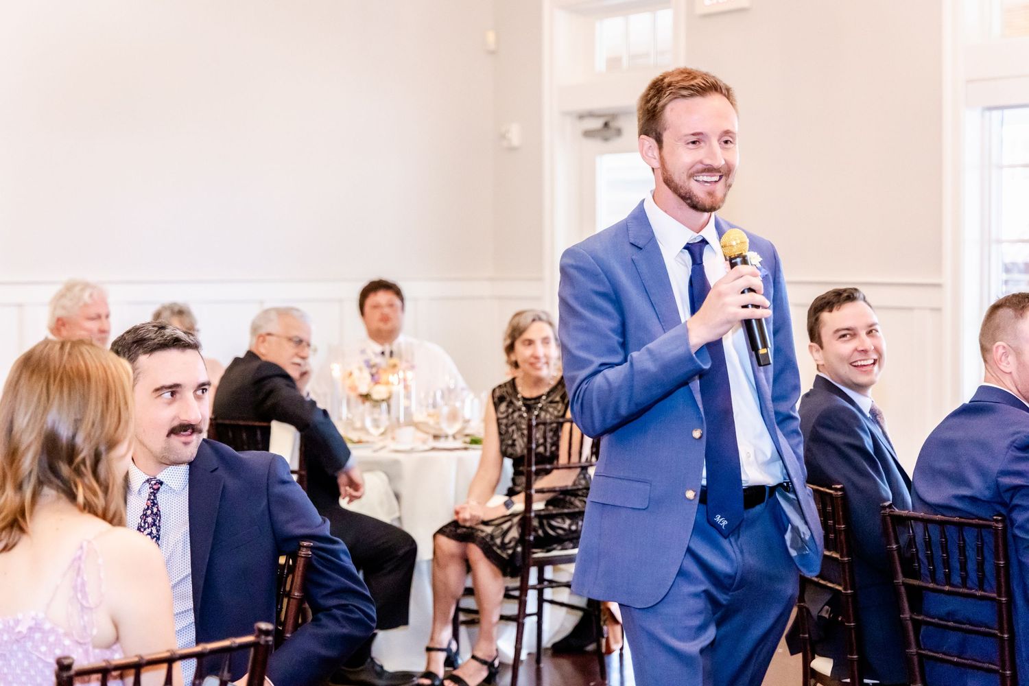 Wedding reception guests seated at tables in an elegant white banquet hall.