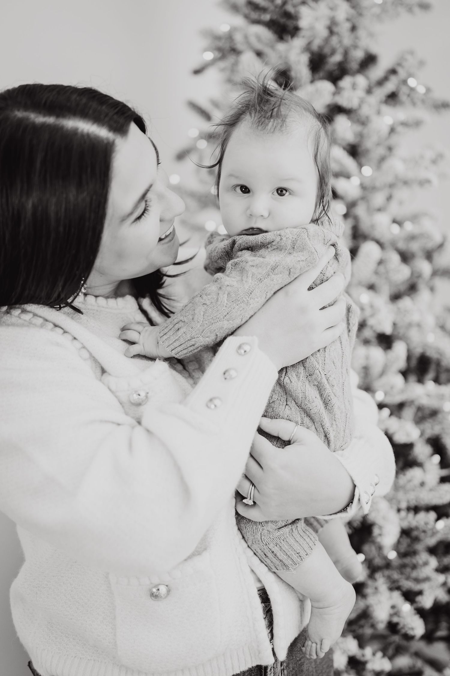 Black and white portrait of a heartwarming parent-child moment by a Christmas tree.
