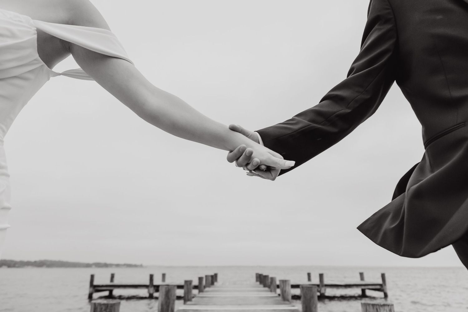 A couple holds hands and dances together in an elegant black and white photograph.