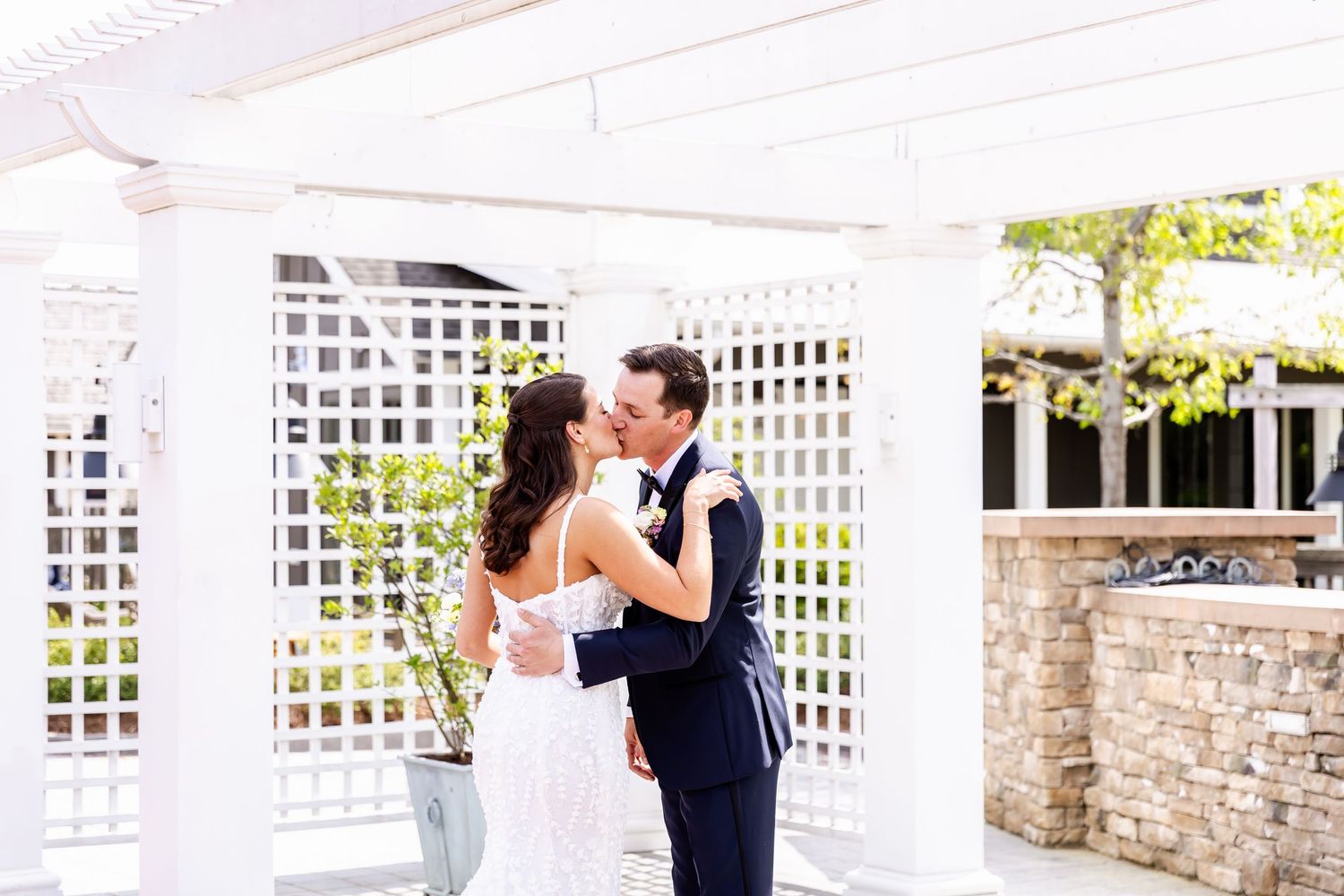 Wedding couple sharing romantic moments under an elegant white pergola.