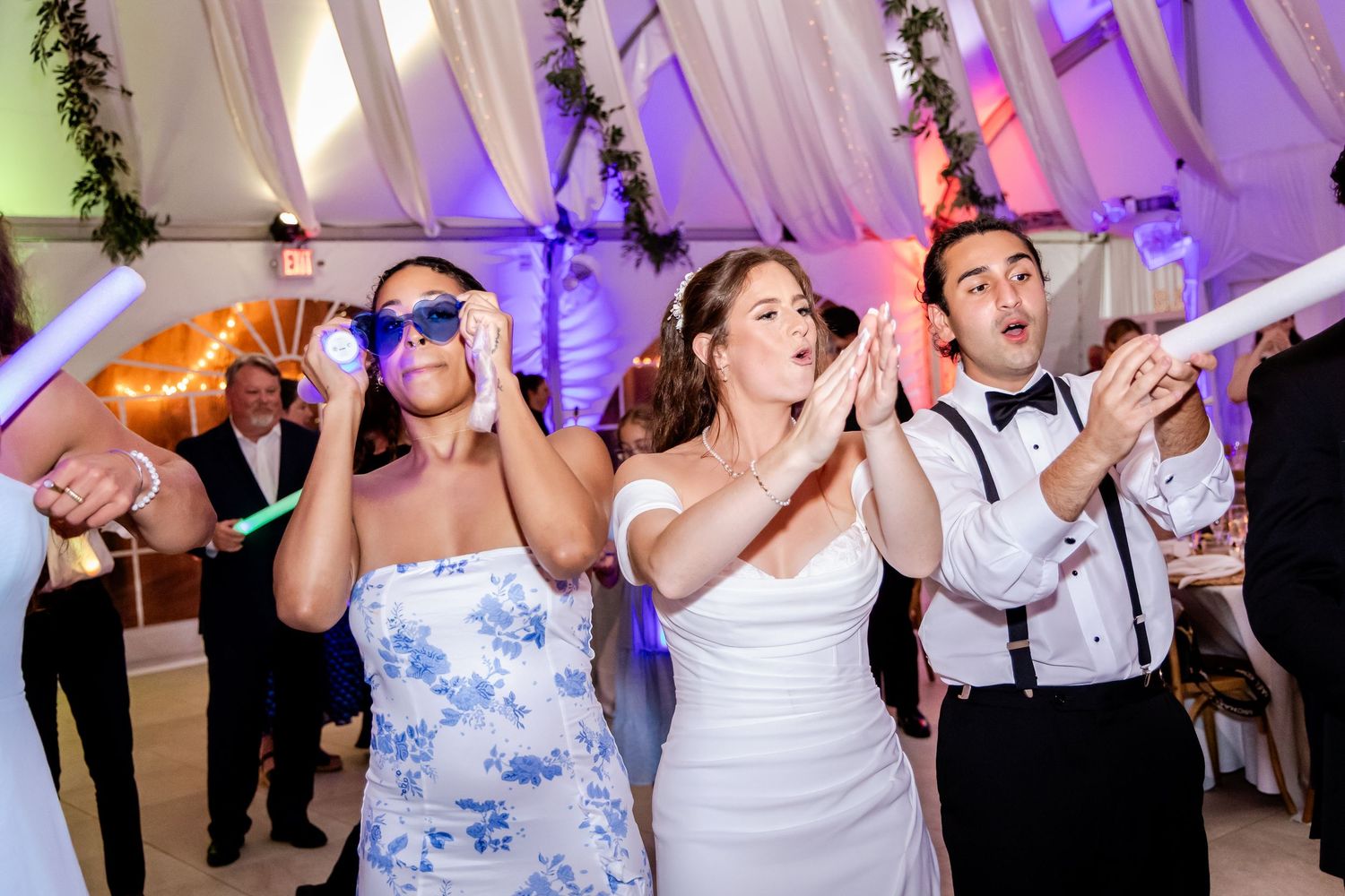 Wedding party guests dancing and celebrating on a colorfully lit dance floor.